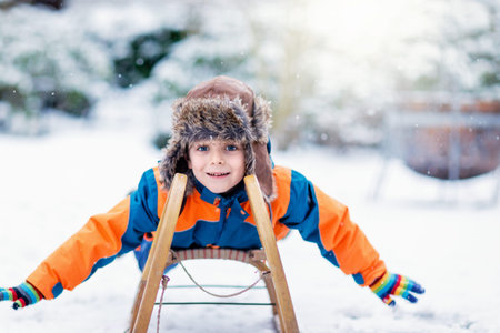 Little kid boy enjoying sleigh ride during snowfall. Happy preschool kid riding on vintage sledge....