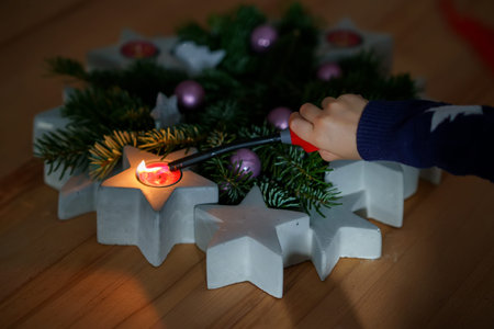 Hand of child lighting a candle on advent wreath on Christmas eve or first advent. Tradtional wreath in Germany. Happy child celebrating family holidayの写真素材