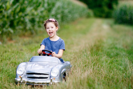 Little preschool kid girl driving big toy car and having fun with driving in natureの写真素材