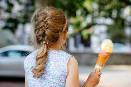 Little preschool girl eating ice cream in waffle cone on sunny summer day. Happy toddler child eat icecream dessert. Sweet food on hot warm summertime days. Bright light, colorful ice-creamの写真素材