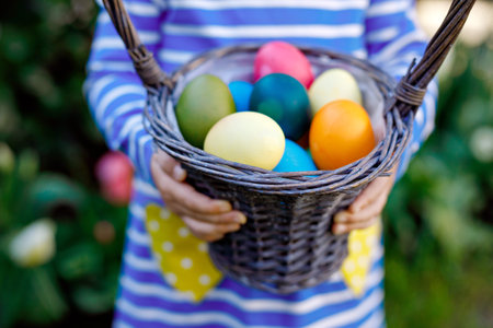 Close-up of of hands of toddler holding basket with colored eggs. Child having fun with traditional Easter eggs hunt, outdoors. Celebration of christian holidayの写真素材