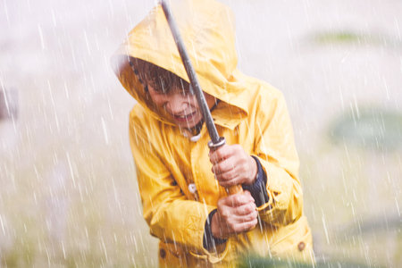 Beautiful little kid boy on way to school walking during sleet, heavy rain and snow with an umbrella on cold day. Happy and joyful child in colorful yellow coat fashion casual clothesの写真素材
