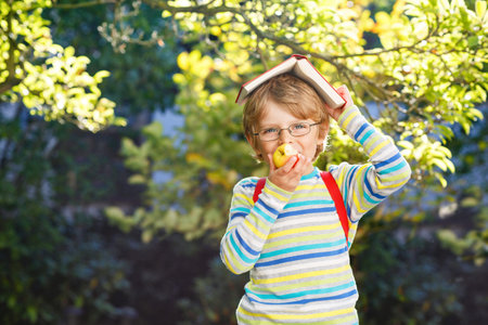 Happy little preschool kid boy with glasses, books, apple and backpack on his first day to school or...