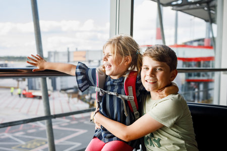 Little girl and school boy at the airport waiting for boarding at big window. Two kids stands at window against the backdrop of airplanes. Happy children, siblings leaving for family summer vacationの写真素材