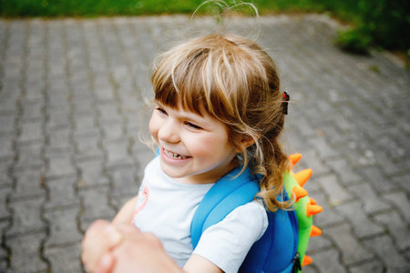Mother accompanies preschool girl to daycare or school. Mom encourages student child to accompany her to school. Caring mother holds daughter hand as she goes to school. Happy positive girl.の写真素材