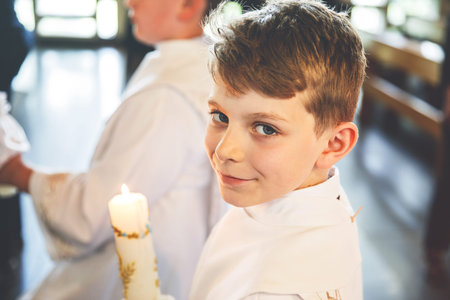 Little kid boy receiving his first holy communion. Happy child holding Christening candle. Tradition in catholic curch. Kid in a white traditional gown in a church near altar.の写真素材