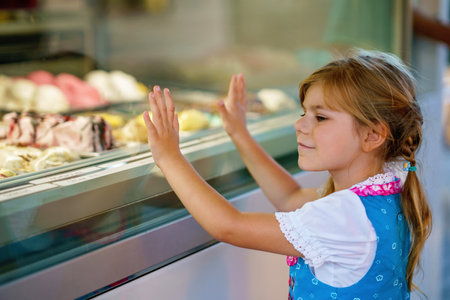 Cute little preschool girl choosing and buying ice cream in outdoor stand cafe. Happy smiling child looking at different sorts of icecream. Sweet summer dessertの写真素材