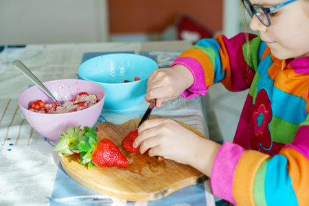 Littl preschool learning how to use a knife cutting strawberry making fruit salad for porridge for breakfast in the kitchen. Healthy food for children.の写真素材