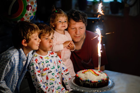 Adorable happy little kid boy celebrating his birthday. Child blowing candles on cake. Father, brother and baby sister sitting together. Happy family.の写真素材