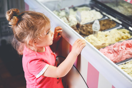 Cute little toddler girl choosing and buying ice cream in a cafe. Happy baby child looking at different sorts of icecream. Sweet home made dessertの写真素材
