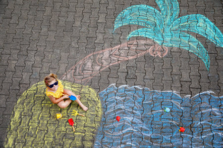 Happy little preschool girl in swimsuit on inflatable ring with sea, sand, palm painted with colorful chalks on asphalt. Cute child with having fun with chalk picture. Summer, vacations, summertimeの写真素材