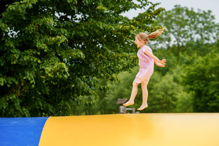 Little preschool girl jumping on trampoline. Happy funny toddler child having fun with outdoor activity in summer. Sports and exercises for children. Trampolin in ukrainian flagg colorsの写真素材