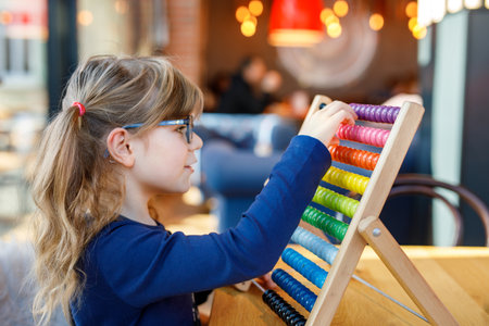 Little preschool girl playing with educational wooden rainbow toy counter abacus. Healthy happy child with glasses learning to count and colors, indoors on sunny day.の写真素材