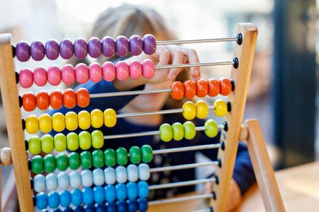 Little preschool girl playing with educational wooden rainbow toy counter abacus. Healthy happy child with glasses learning to count and colors, indoors on sunny day.の写真素材