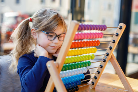 Little preschool girl playing with educational wooden rainbow toy counter abacus. Healthy happy child with glasses learning to count and colors, indoors on sunny day.の写真素材