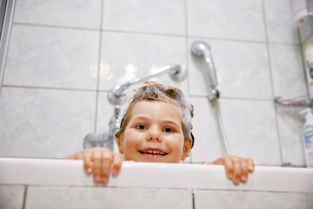 Cute child with shampoo foam and bubbles on hair taking bath. Portrait of happy smiling preschool...