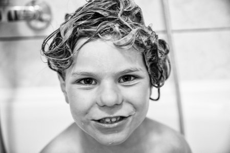 Cute child with shampoo foam and bubbles on hair taking bath. Portrait of happy smiling preschool girl health care and hygiene concept. Washes hair by herself.の写真素材