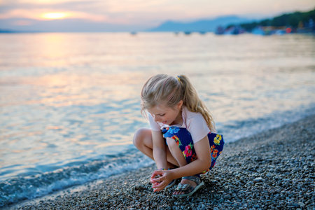 Little girl walking on beautiful ocean beach. Happy preschool child play by sunset on sea beach. Family vacations with children in summer.の写真素材