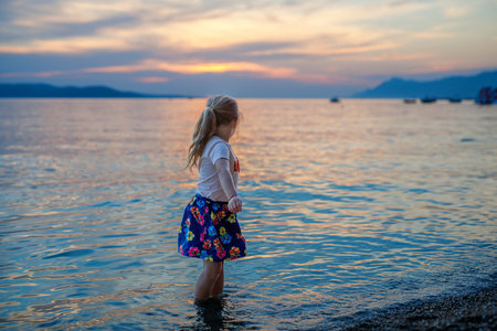 Little girl walking on beautiful ocean beach. Happy preschool child play by sunset on sea beach. Family vacations with children in summer.の写真素材