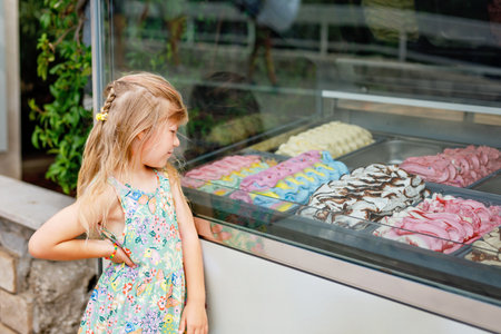 Happy preschool girl choosing and buying ice cream in outdoor stand cafe. Cute child looking at different sorts of icecream. Sweet summer dessert on family vacations. Summertime.の写真素材