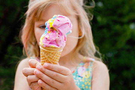 Happy preschool girl eating colorful ice cream in waffle cone on sunny summer day. Little toddler child eat icecream dessert. Sweet food on hot warm summertime days. Bright light, colorful ice-creamの写真素材