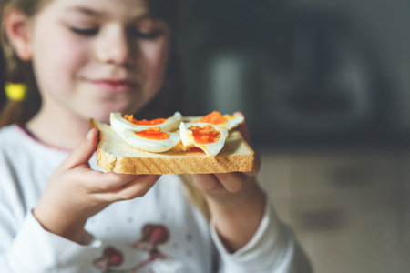 Little smiling girl have a breakfast at home. Preschool child eating sandwich with boiled eggs. Happy children, healthy food and meal.の写真素材