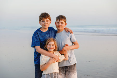 Three kids standing on beach at sunset. happy family, two school boys and one little preschool girl. Siblings having fun.の写真素材