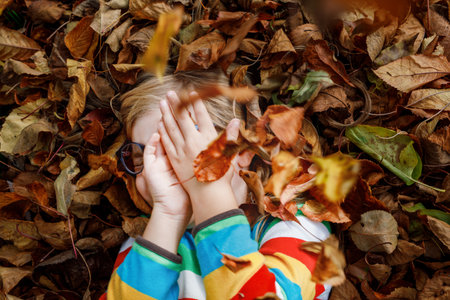 Fall portrait of little preschool girl in autumn park on warm october day with oak and maple leaf. Child with lot of leaves. Family outdoor fun in fall. Kid smiling. Healthy funny child with glassesの写真素材