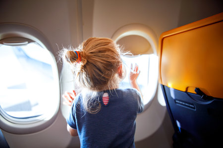 Adorable little girl traveling by an airplane. Child sitting by aircraft window and looking outside. Traveling with kids abroad. Family on summer vacations.の写真素材