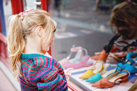 Little Girl looks at the window near the shopping center. Adorable happy child looking on shoes in store window.の写真素材