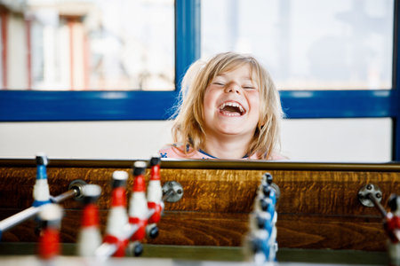 Little preschool girl playing table soccer. Happy excited positive child having fun with family game with siblings or friends.の写真素材