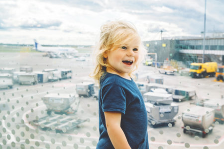 Cute little toddler girl at the airport, traveling. Happy healthy child waiting near window and...