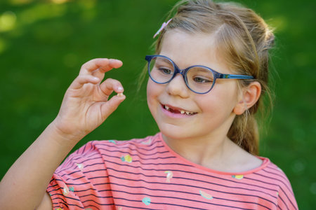 Portrait of a cute preschool girl with eye glasses and big teeth gap outdoors in park. Happy funny...