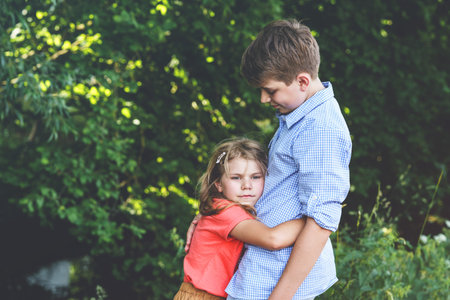An upset little girl finds comfort in the embrace of her caring teenage brother, exemplifying the...