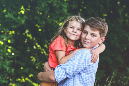 Happy Little Girl Embraces Her Loving Brother, Teenager Boy, Showcasing the Warmth and Love within Their Family Bond. Carefree Childhood, Brother and Sister Bonding.の写真素材