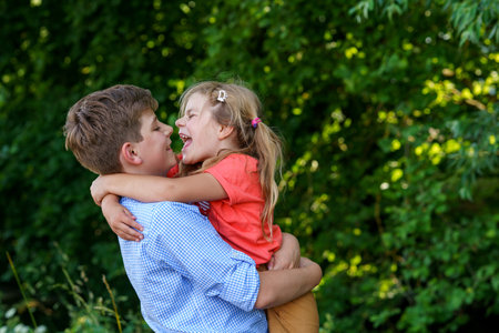 Happy Little Girl Embraces Her Loving Brother, Teenager Boy, Showcasing the Warmth and Love within Their Family Bond. Carefree Childhood, Brother and Sister Bonding.の写真素材