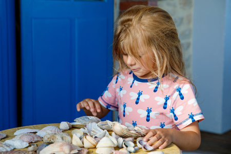Little preschool girl with variation of different shells and clams at home. Happy child with collected shell from Normandy, France. Children, education, vacation concept.の写真素材