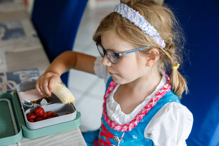Cute Little Girl with Eyeglasses Eating Sandwich and Fruits during Break between Classes. Healthy unhealthy food for kids. Breakfast Lunch Box for Children at Schoolの写真素材