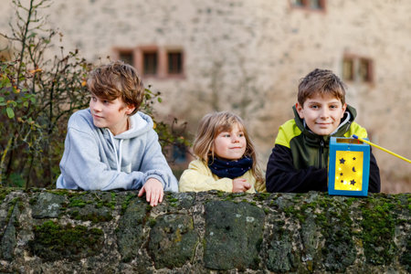 Little toddler girl and two kids boys holding selfmade lanterns with candle for St. Martin procession. Three healthy children happy about family parade in kindergarten. German tradition Martin parade.の写真素材