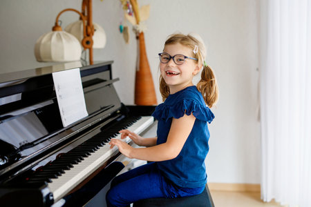 Beautiful little preschool girl playing piano at music school. Cute child having fun with learning to play music instrument. Early musical education for childrenの写真素材