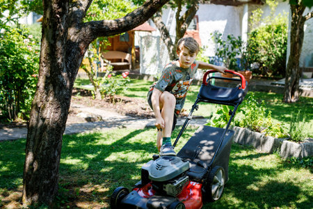 Happy preteen kid boy with lawn mower. Portrait of smiling teenager child working in garden,...