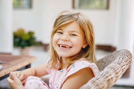 Cute preschool girl in nightgown sitting at breakfast table with family in summer garden. Happy child smiling and having fun.の写真素材