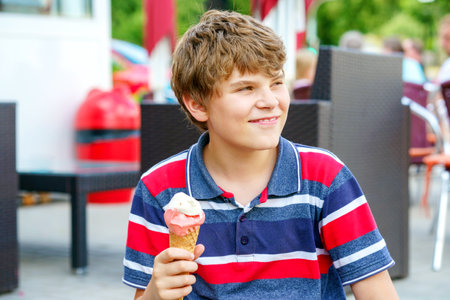 Cheerful laughing preteen boy eating multicolored ice cream in a waffle cone. Cool in the summer heat.Sweet snack for children. Happy child.の写真素材