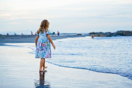 Happy Child, Little Preschool Girl in Dress Running And Jumping In The Waves During Summer Vacation On Exotic Tropical Beach by Sunset. Family Journey On Ocean Coast.の写真素材