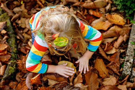 Fall portrait of little preschool girl in autumn park on warm october day with oak and maple leaf. Child with lot of leaves. Family outdoor fun in fall. Kid smiling. Healthy funny child with glassesの写真素材
