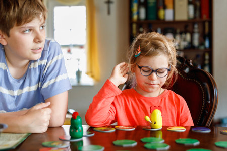 Family playing board game at home. Kids play strategic game. Little sister girl and school brother boy. Fun indoor activity. Siblings bond. Educational toys.の写真素材