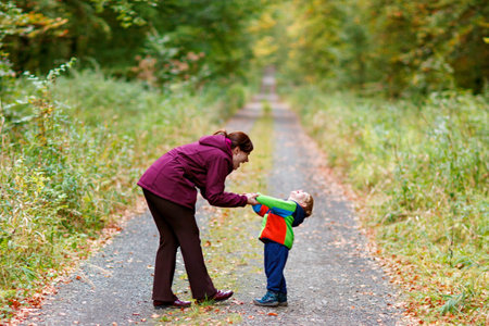 Little boy with his young mother in the autumn orest. Active family time on nature. Fun with little kids in fall days. Mum and toddler son walking in forest.の写真素材