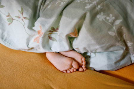 Childs legs are covered with white bed linen. The warmth of home comfort. Feet of little small girl.の写真素材
