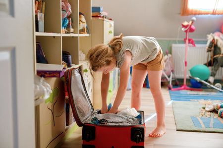 Little girl packing suitcase at home. Cute child putting clothes into suitcase. Preparing for family vacations with children. Practicing independenceの写真素材