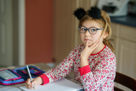 Little schoolgirl doing homework at home. Cute happy child learning to write, primary class. Girl...